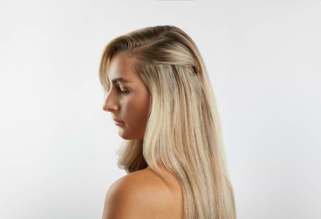 Profile of a woman with long, straight blonde hair extensions against a plain white background.