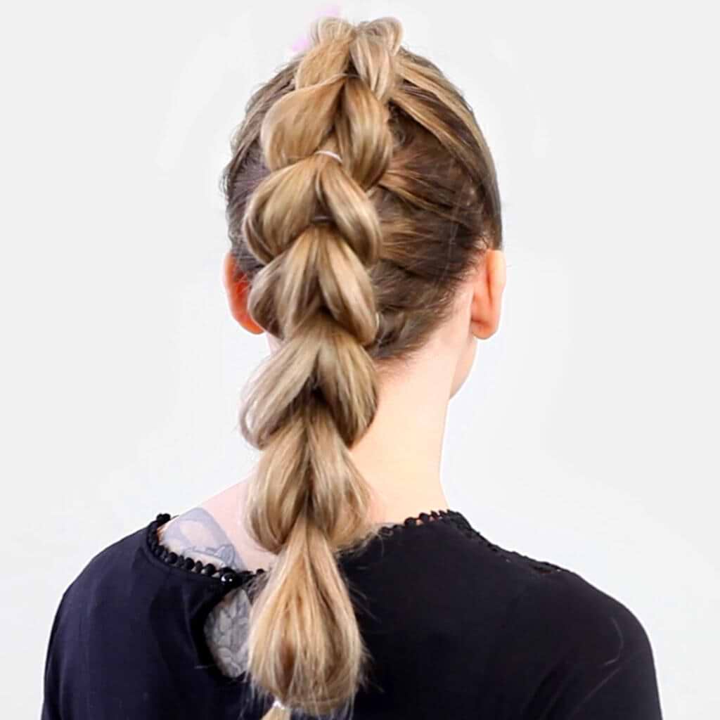 Back view of a person with a thick, blonde hair extensions in Dutch braid, wearing a black top with a slightly frayed neckline.