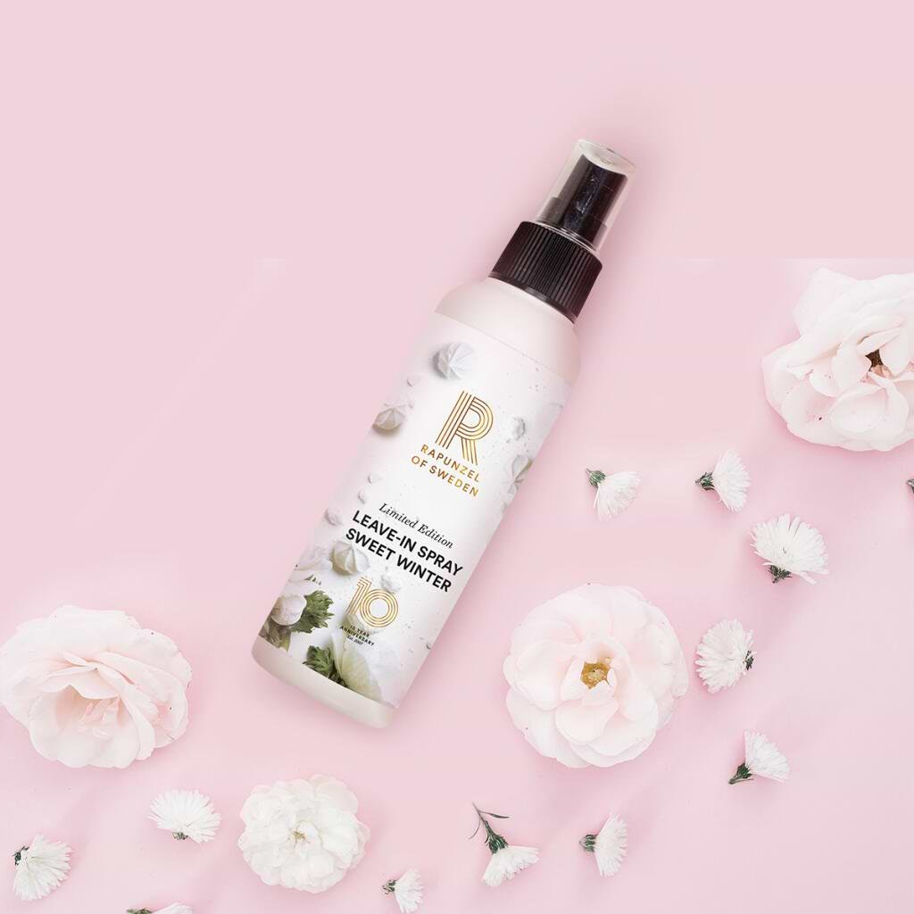 A bottle of "Leave-In Spray Sweet Winter" on a pink background, surrounded by white and pink flowers.