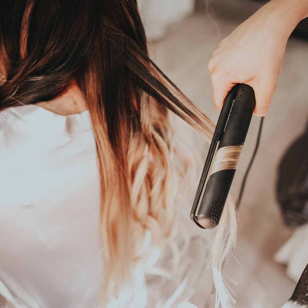 A person straightens long, wavy hair extensions with a flat iron, creating a smooth, sleek look.