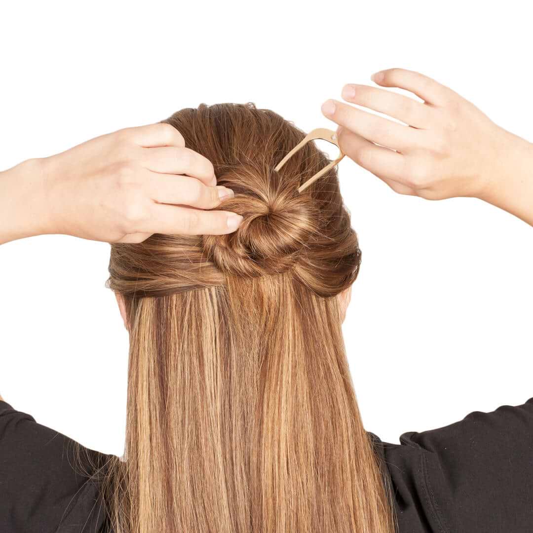 Person with long brown hair extensions creating a twisted bun using a hairpin, against a white background.