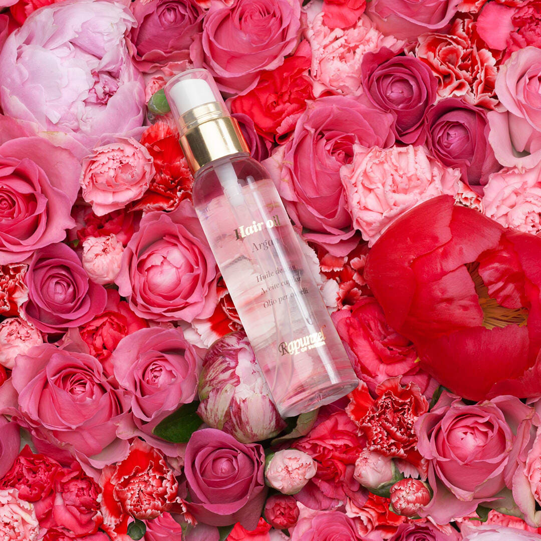 A bottle of facial mist lies on a bed of pink and red roses and peonies, creating a vibrant and luxurious floral display.
