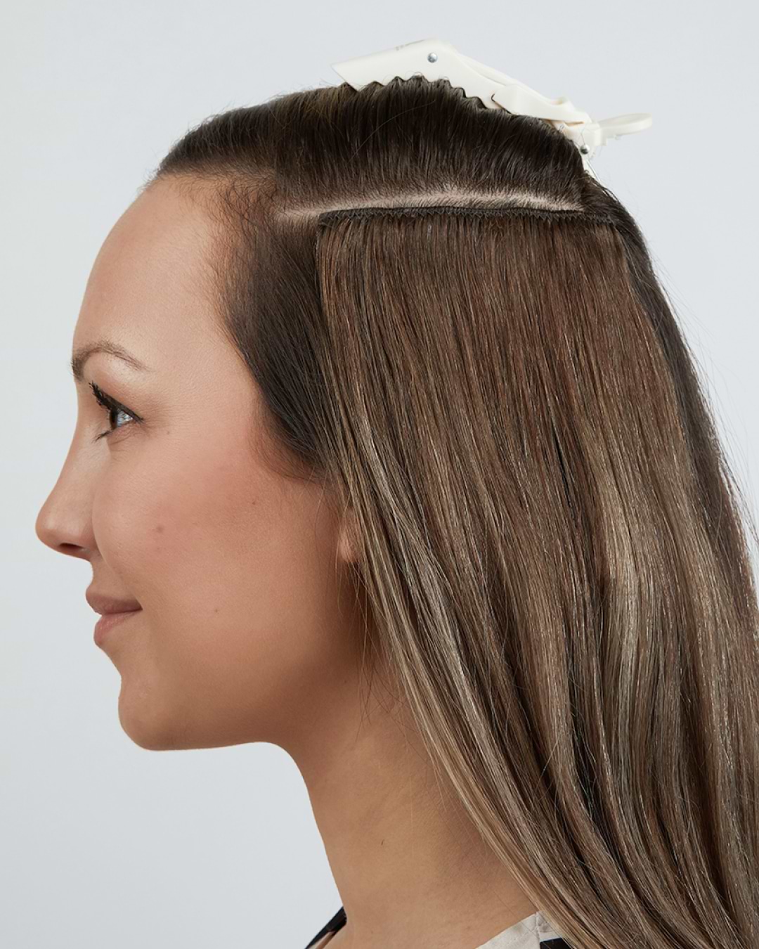 Profile of a woman with long brown hair, partially clipped up, against a plain background.