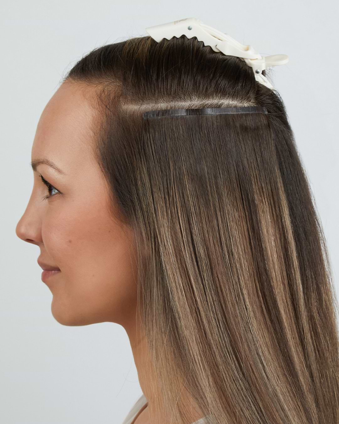 Woman with long, straight hair getting hair extensions; section clipped on top, extensions visible underneath.