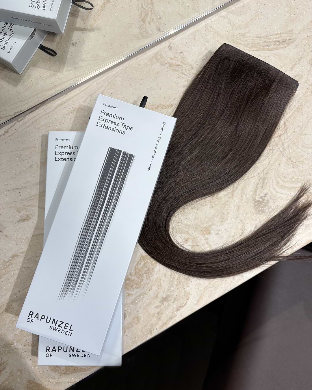 Premium Express Tape Hair Extensions beside Rapunzel of Sweden packaging on a marble surface.