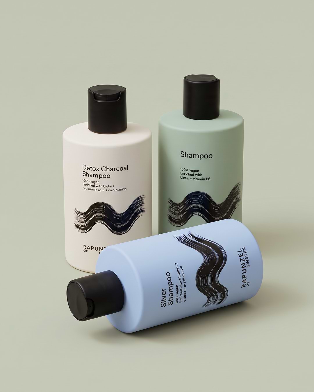 Three bottles of shampoo with black caps on a light green background, labeled Detox Charcoal, Silver, and Vegan Shampoo by Rapunzel of Sweden.