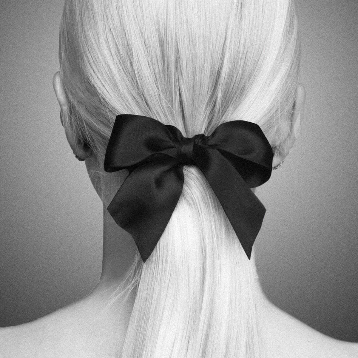 A person with long, straight hair extensions tied in a low ponytail with a large black bow, viewed from the back in black and white.