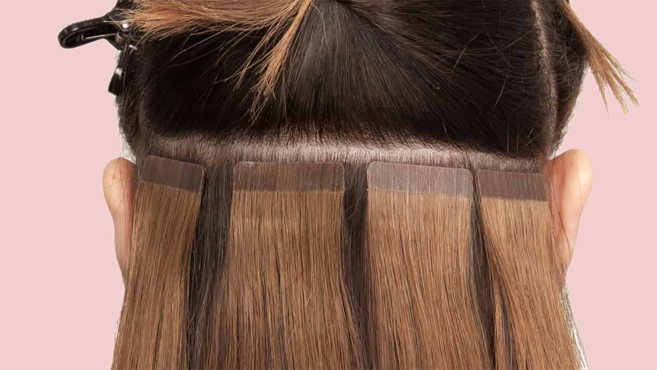 Hair extensions being applied to the back of a person's head, showing several sections attached near the roots.