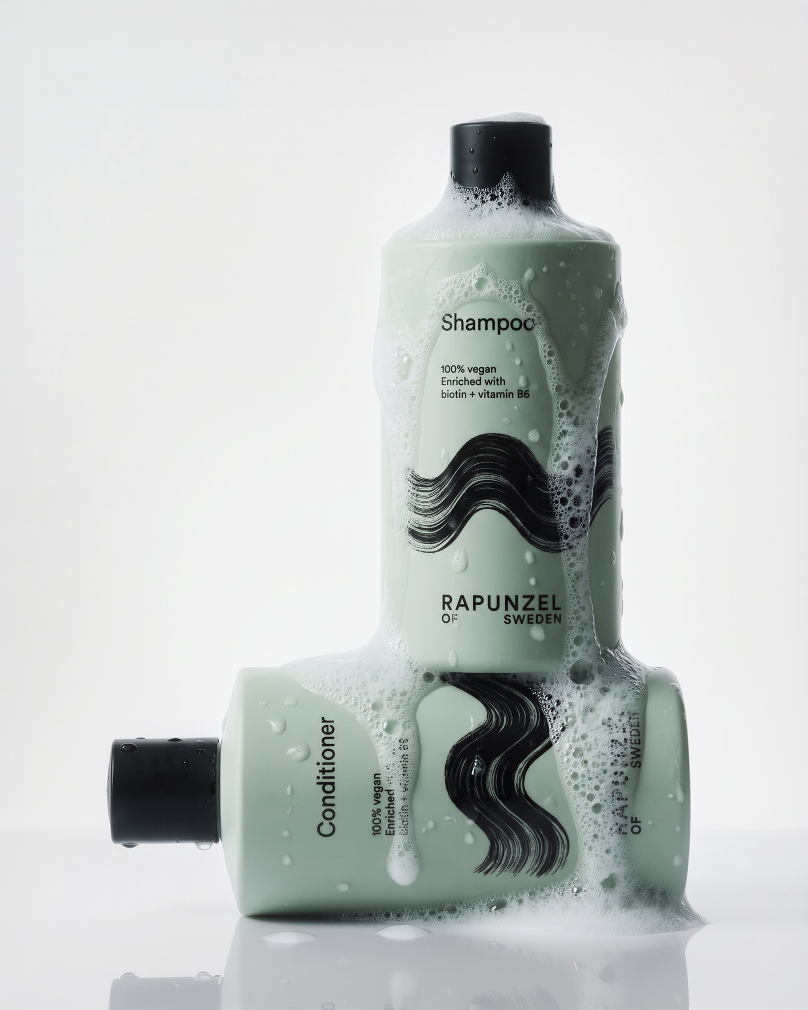 Two bottles of Rapunzel of Sweden shampoo and conditioner, covered in suds, with labels indicating they're 100% vegan and enriched with biotin and vitamin B6.