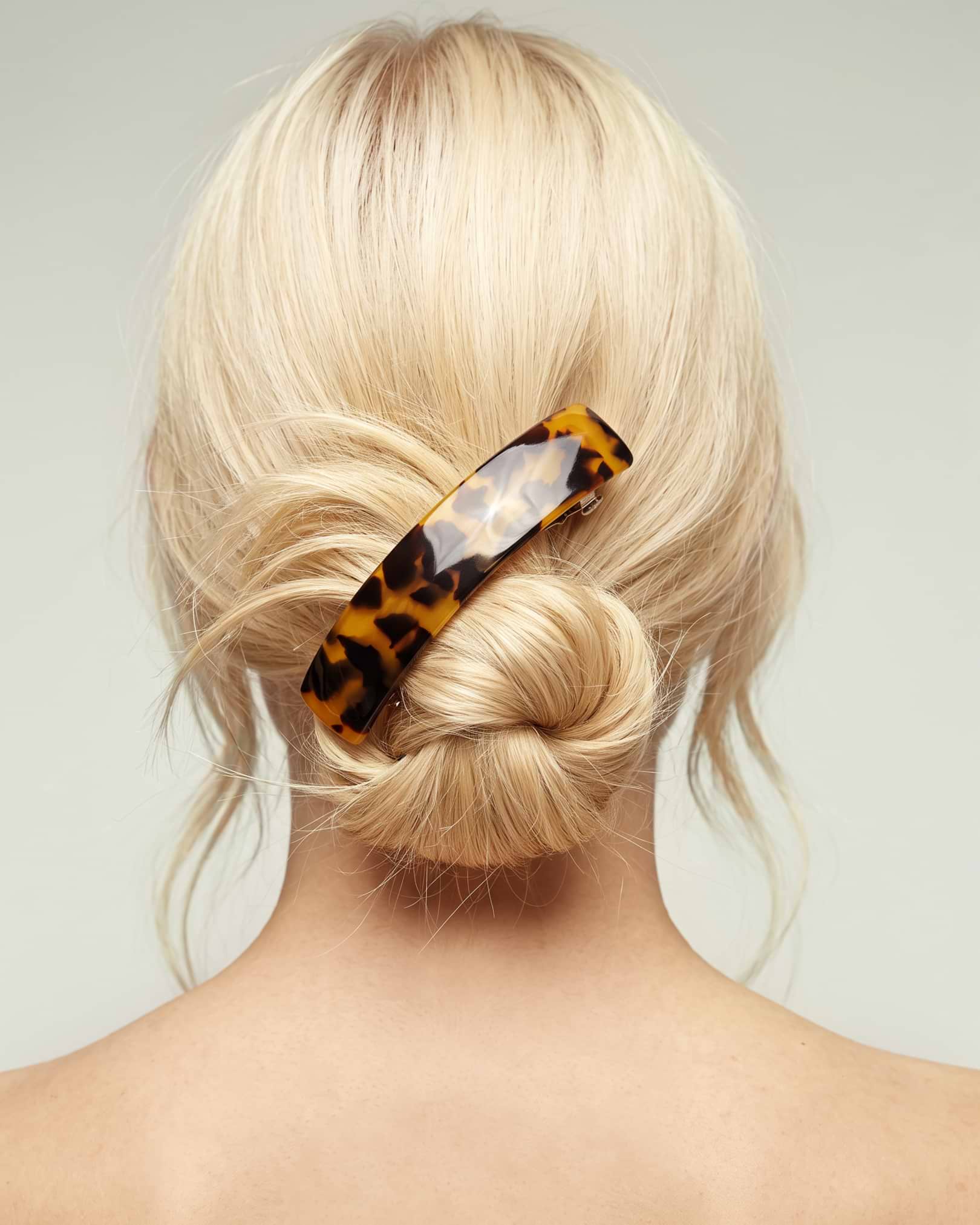 Blonde hair styled in a bun secured with a tortoiseshell-patterned hair barrette, viewed from the back.