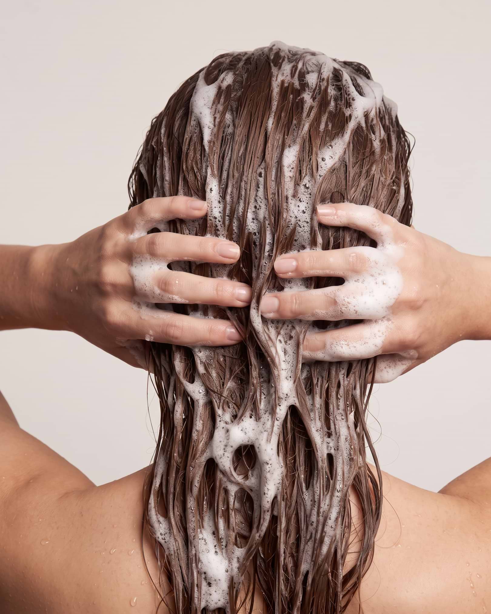 Person washing their hair with shampoo, hands massaging scalp, visible suds and wet hair strands.