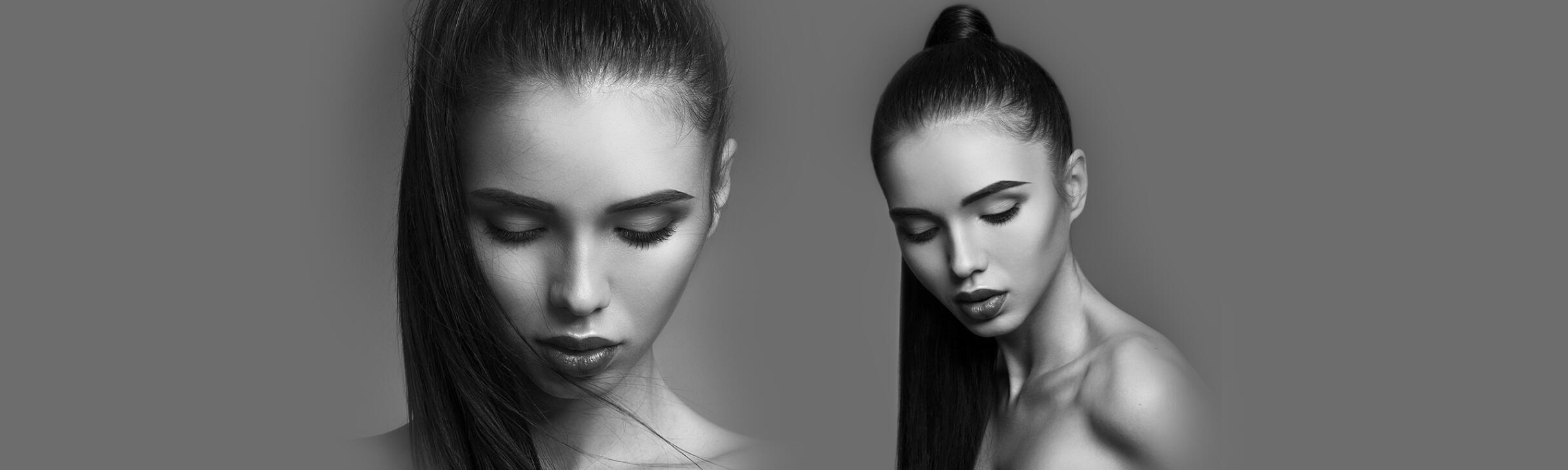 Black and white image of a woman with long, sleek hair extensions in a ponytail, looking down with a serene expression against a gray background.