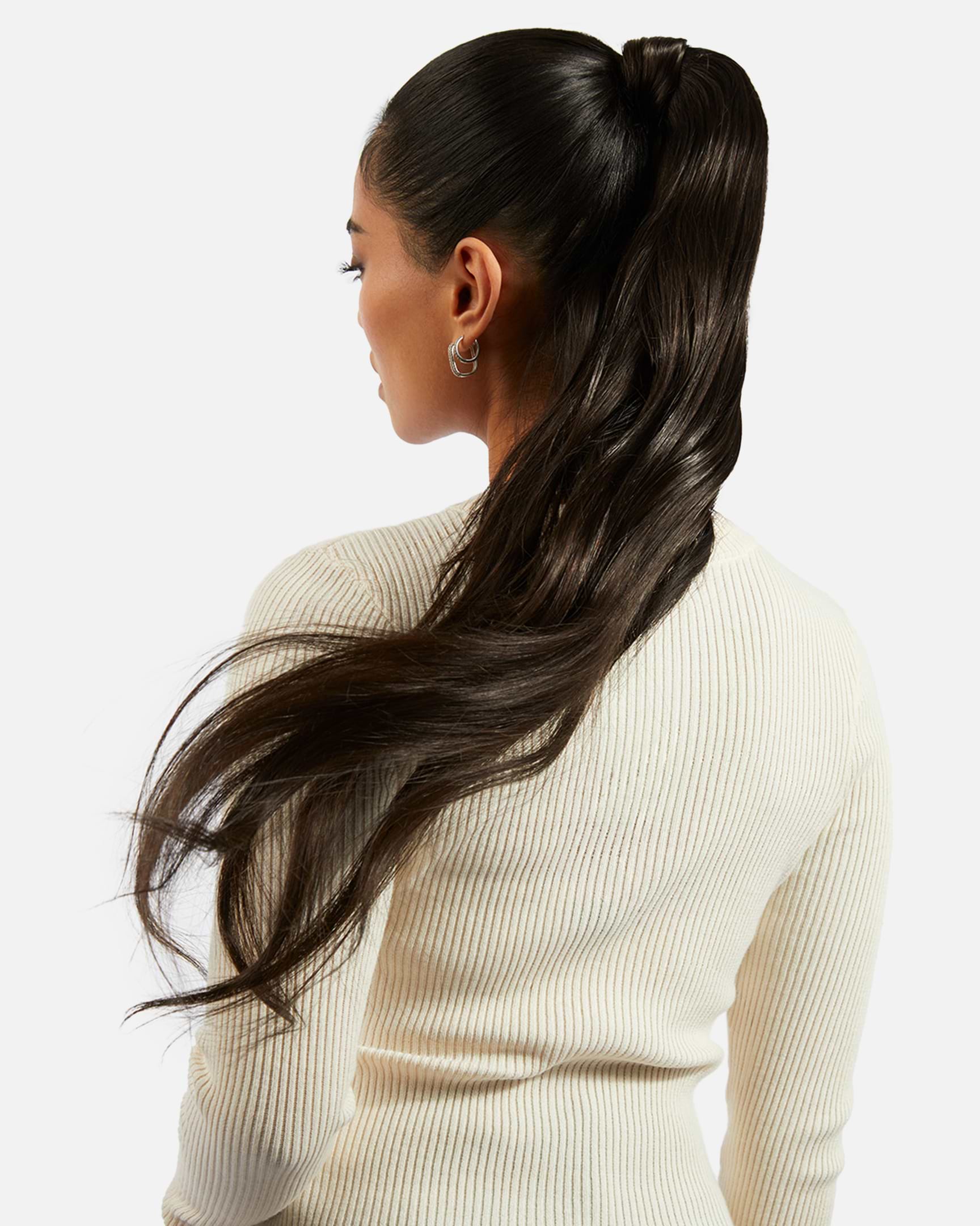 A person with a sleek, high ponytail extension and long, dark hair, wearing a ribbed white top, is seen from the back against a plain background.