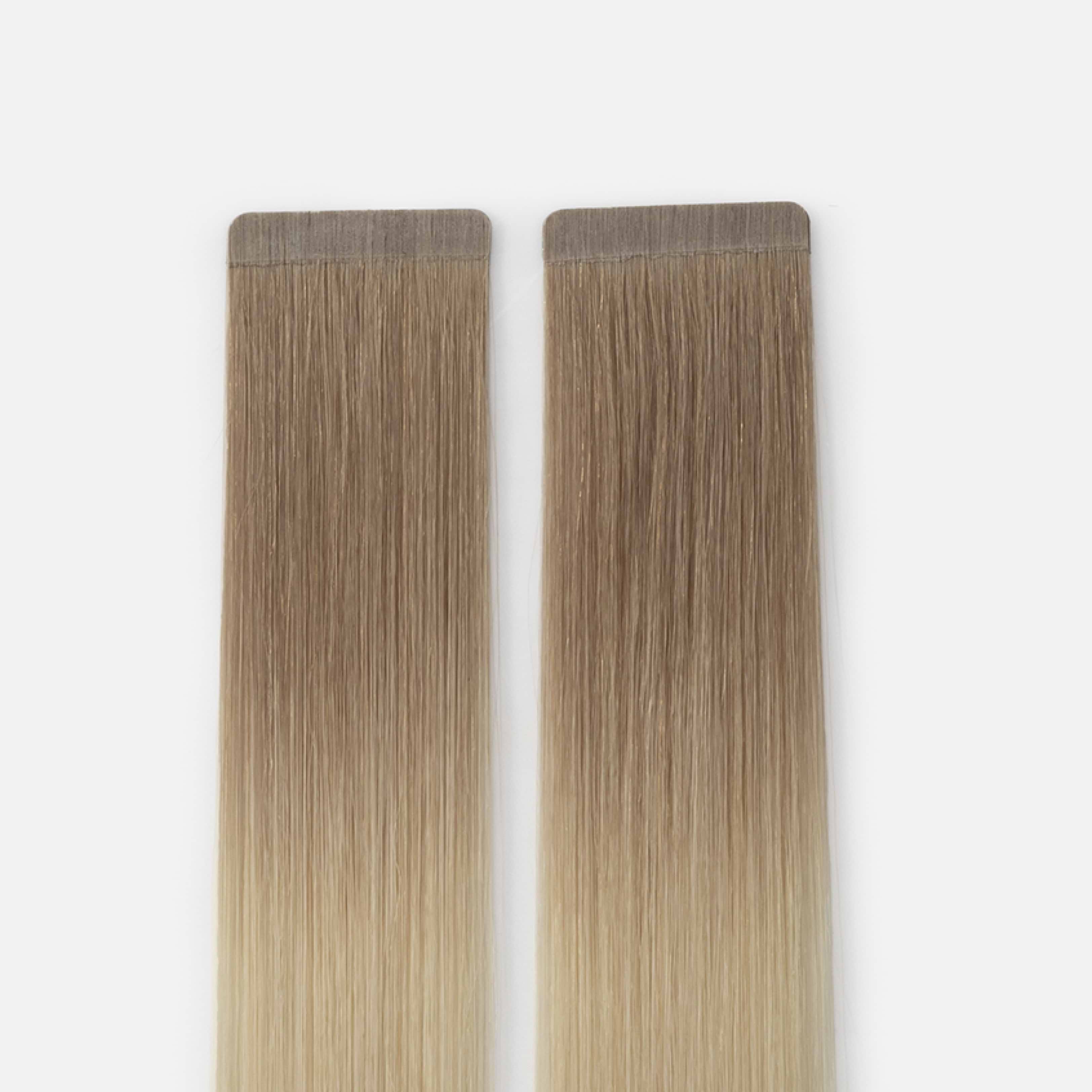 Two straight, ombre hair extensions with a seamless tape-in design, transitioning from light brown to blonde, against a plain background.