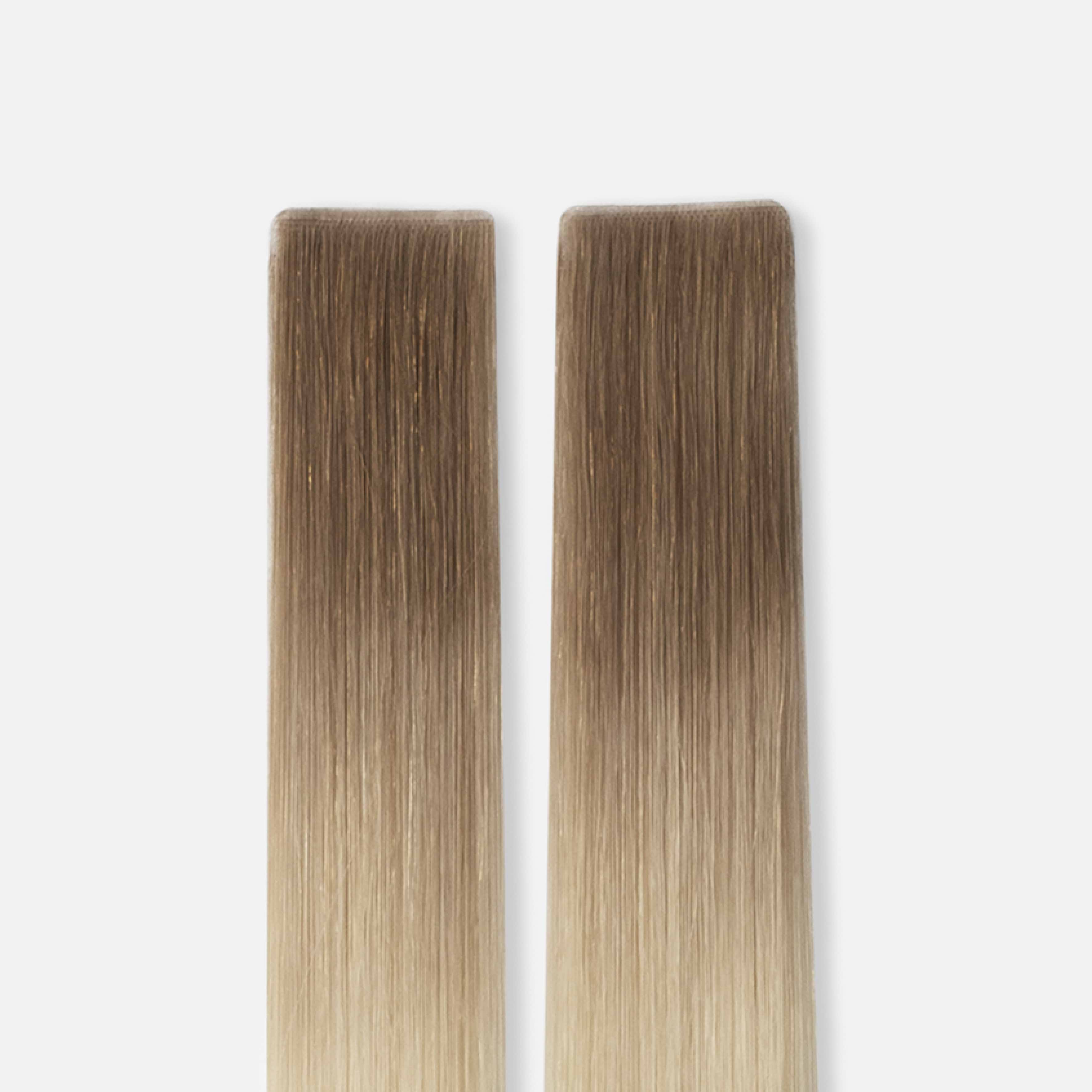 Two straight, rectangular strips of ombre hair extensions, transitioning from dark brown to light blonde, against a plain white background.