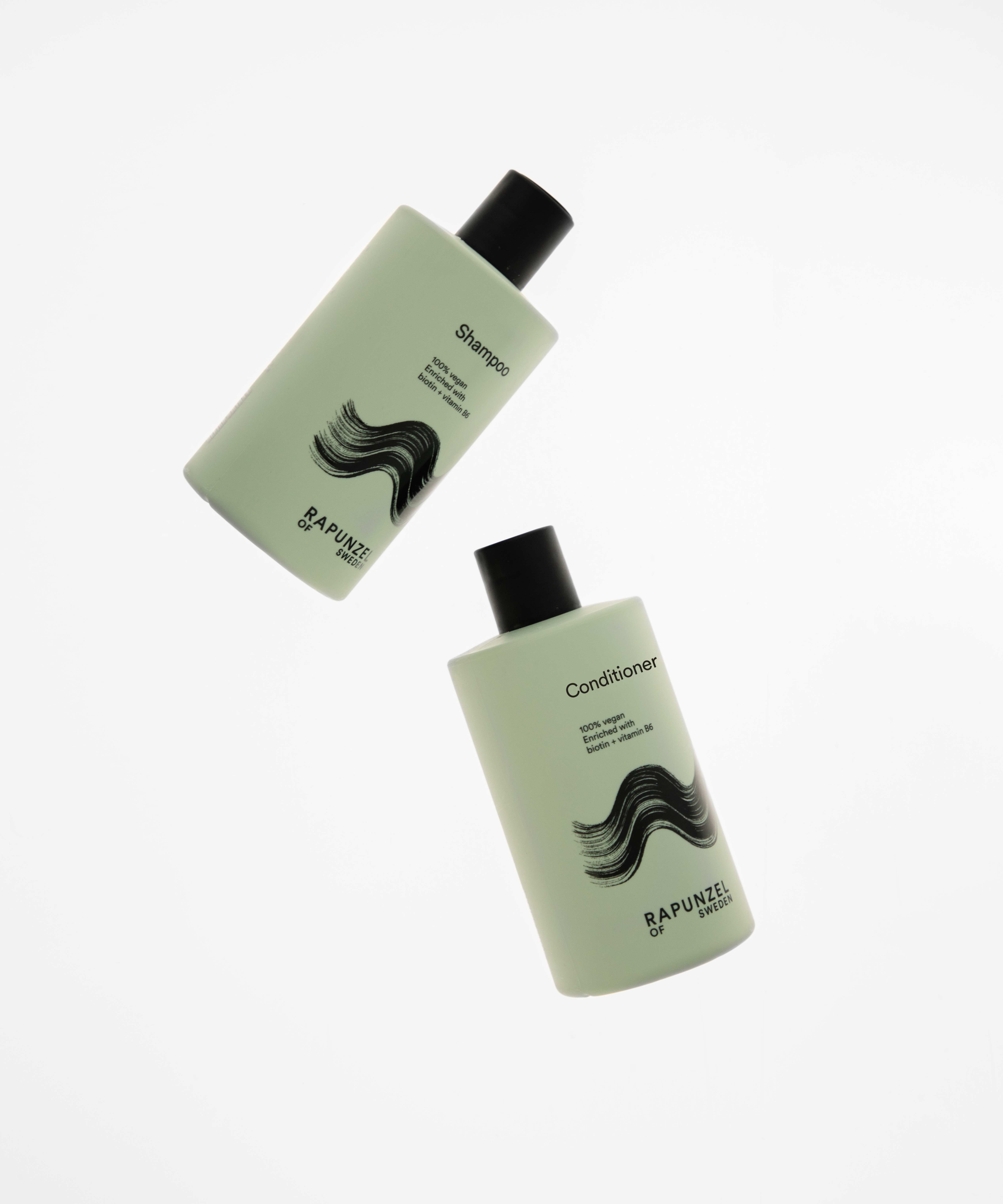 Two light green bottles of shampoo and conditioner with black caps, featuring a wavy hair design, floating against a white background.