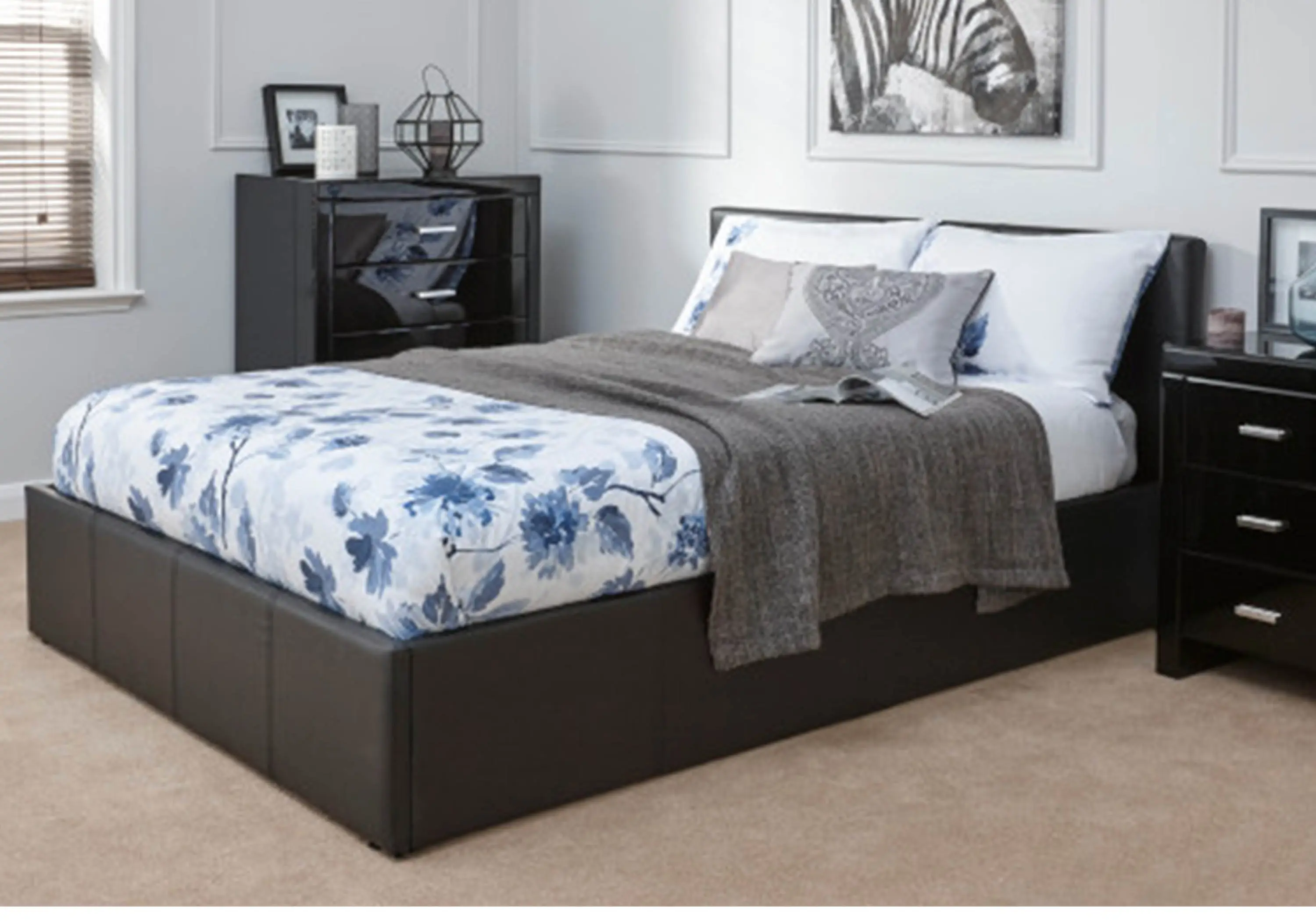 Brown small double ottoman bed, which has white bedsheets with blue flowery pattern on them