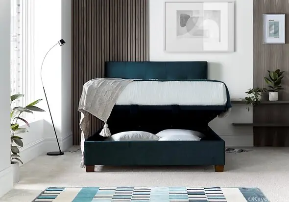 Luxurious deep blue velvet ottoman bed frame with modern dark wooden feet.