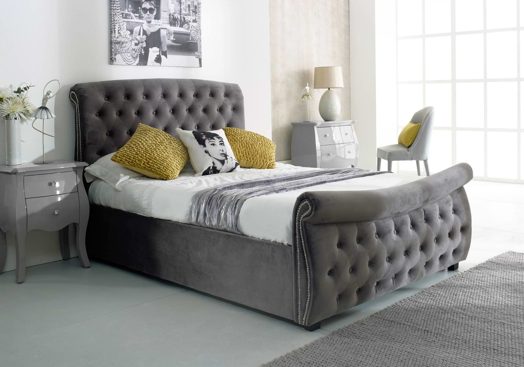 Grey ottoman bed with grey and white sheets, yellow pillows, and a pillow with a portait of Audery Hepburn