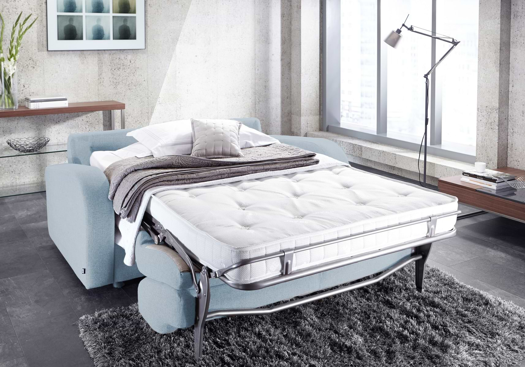 Blue sofa bed folded out into bed form, with white and brown sheets