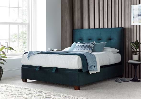Luxurious deep blue velvet ottoman bed frame with modern dark wooden feet.