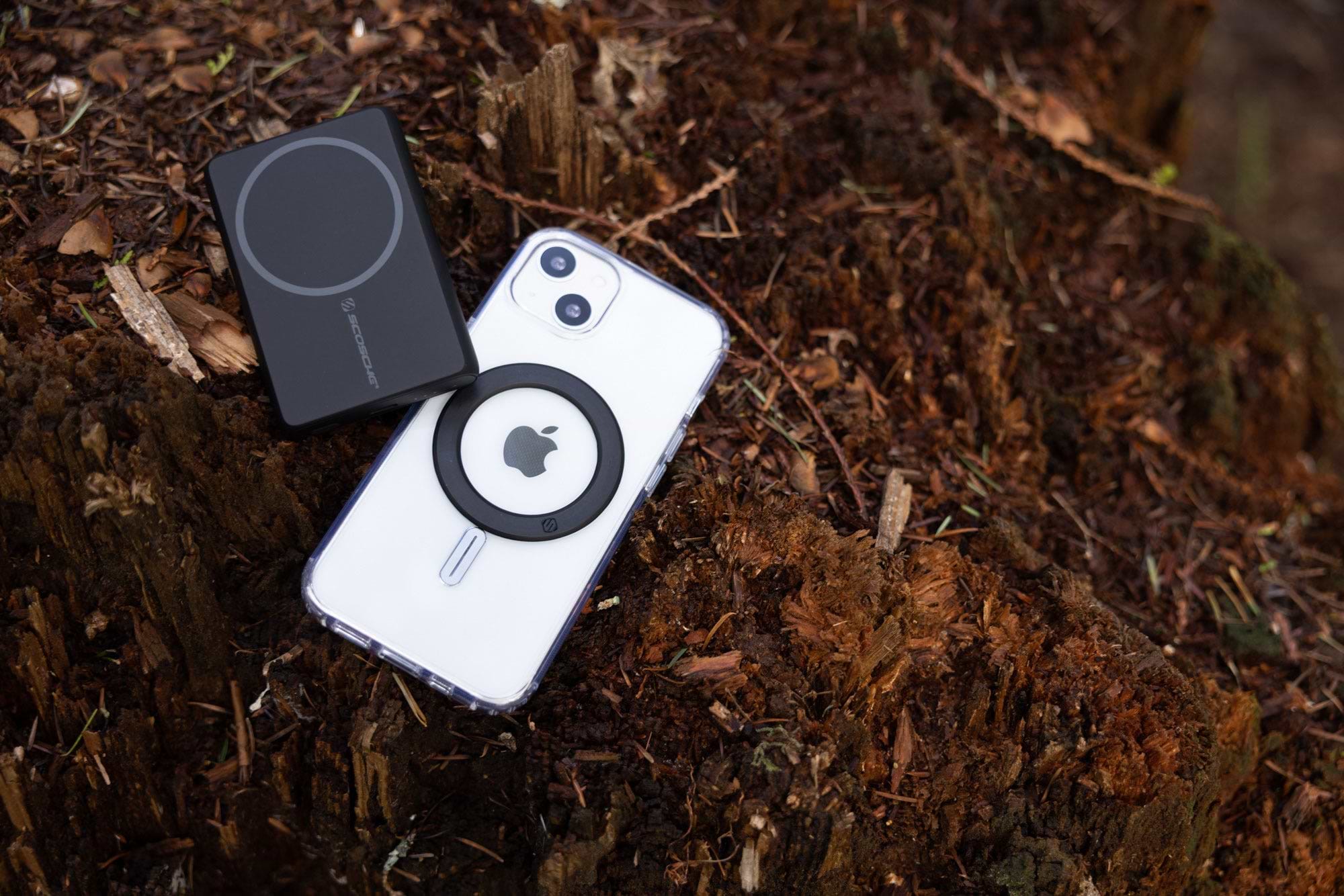 iphone with magic ring adapter next to magsafe portable power bank while laying in forest floor