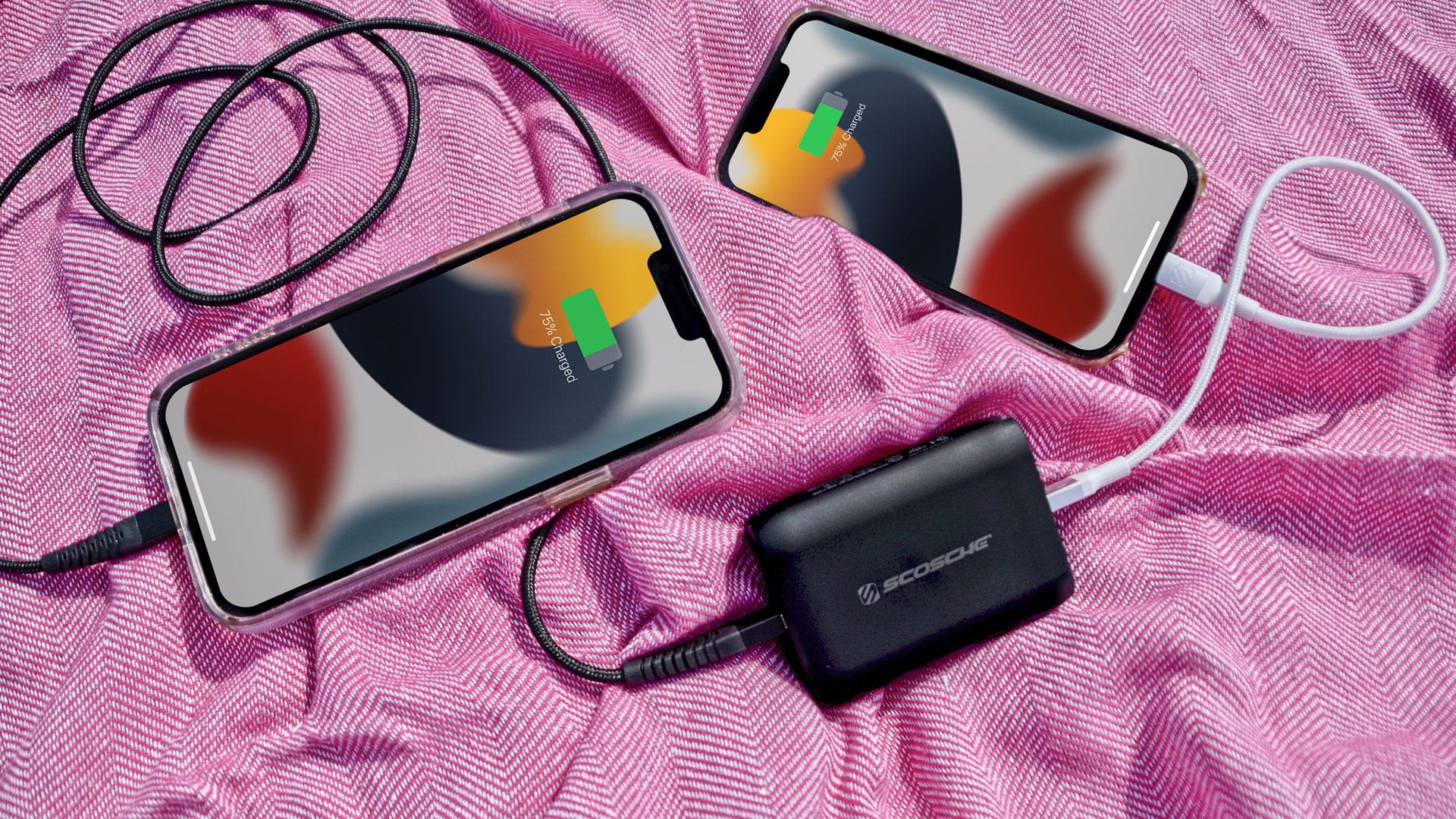 2 iphones charging via Scosche power bank connected via Scosche charging cables while placed on pink patterned background