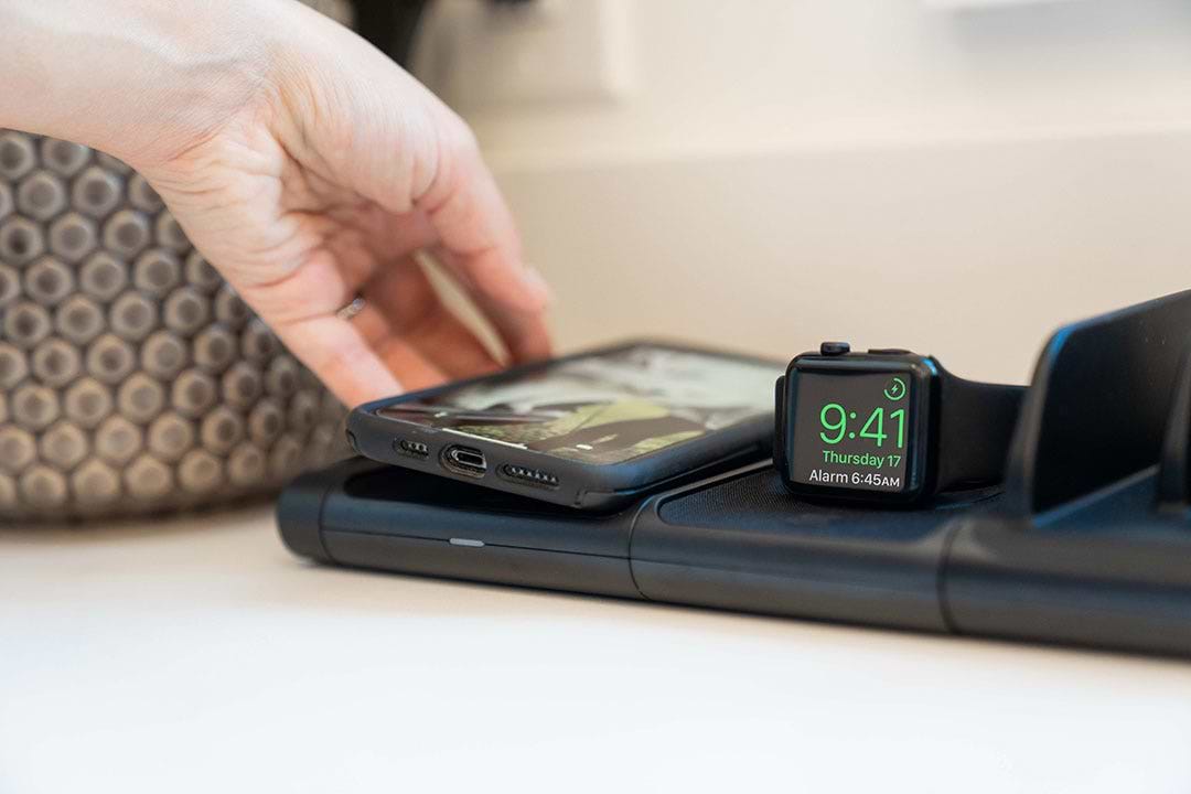 Woman placing iphone on wireless charging pad next to apple watch charging on wireless charger