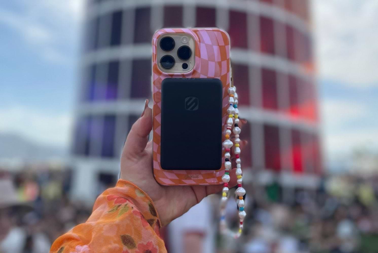 Woman's hand holding iphone with case and Scosche mag safe power bank with building in background