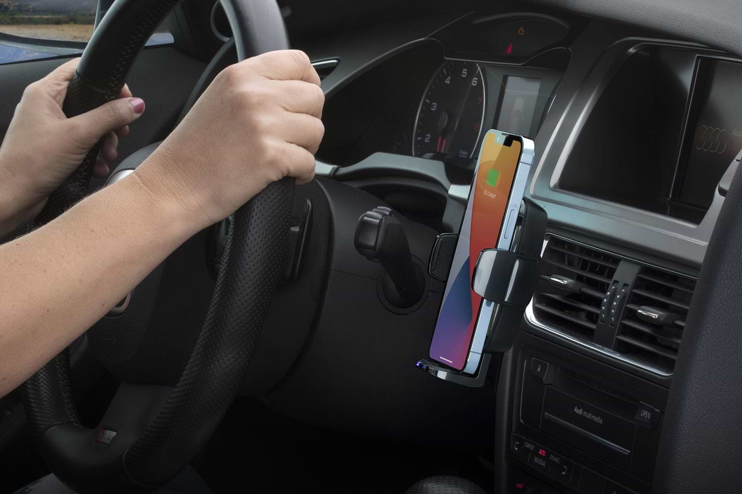 Woman with hands on steering wheel with phone sitting in phone mount on car vent