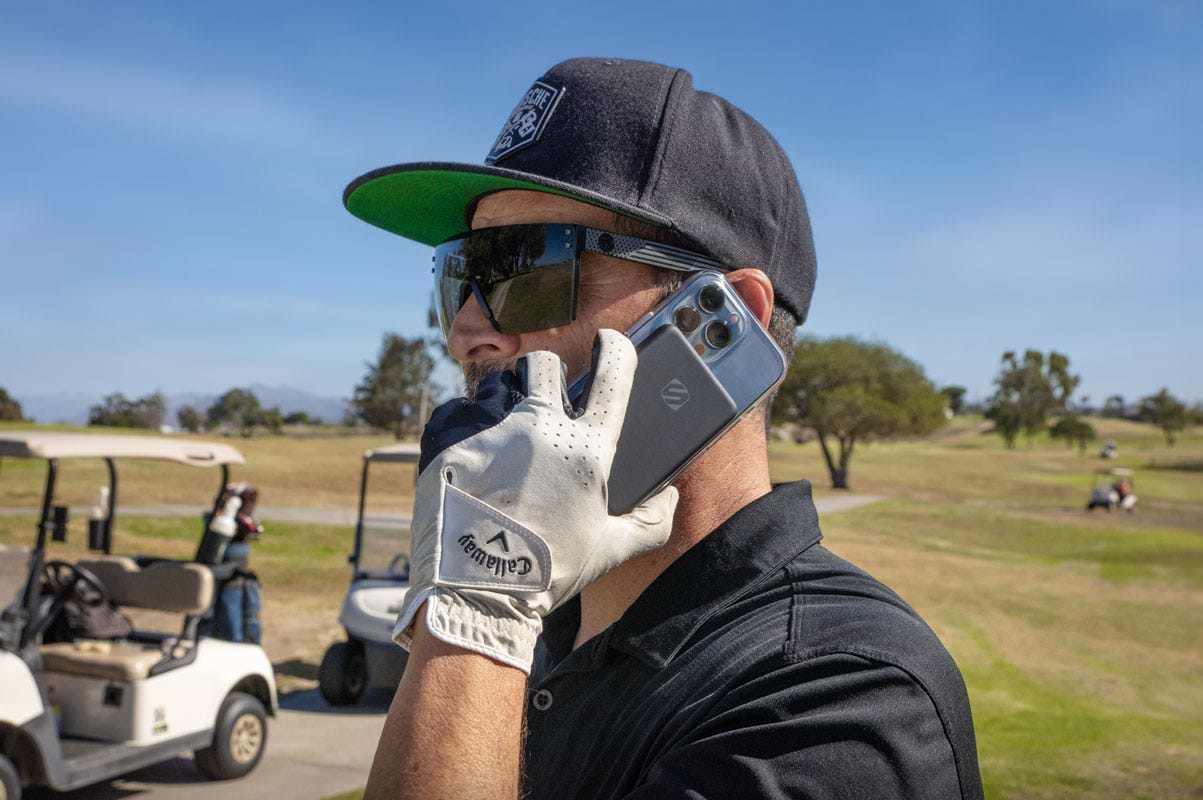 man talking on iphone with portable power bank attached while playing golf