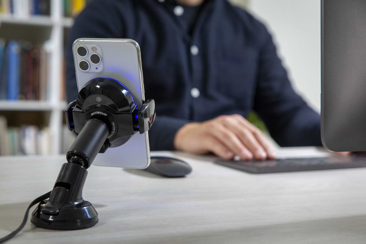 iphone charging via Scosche magic grip wireless charging mount on desk with man sitting at computer in background