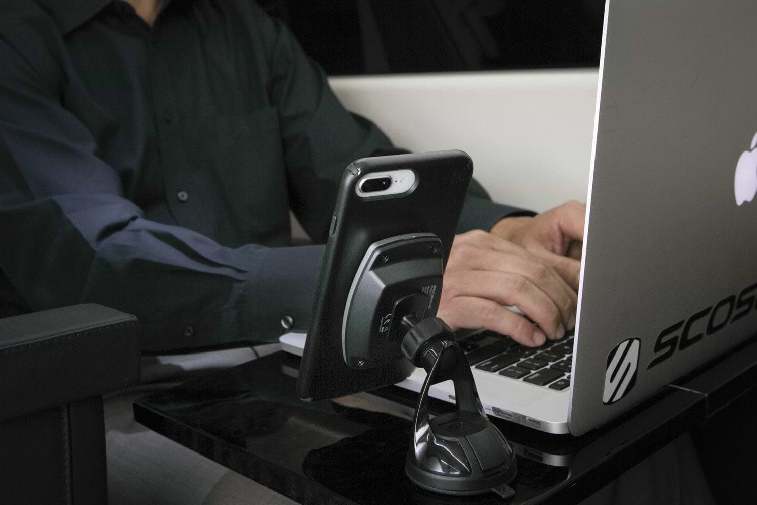 man typing on laptop with phone charging via Scosche MagSafe wireless charging mount