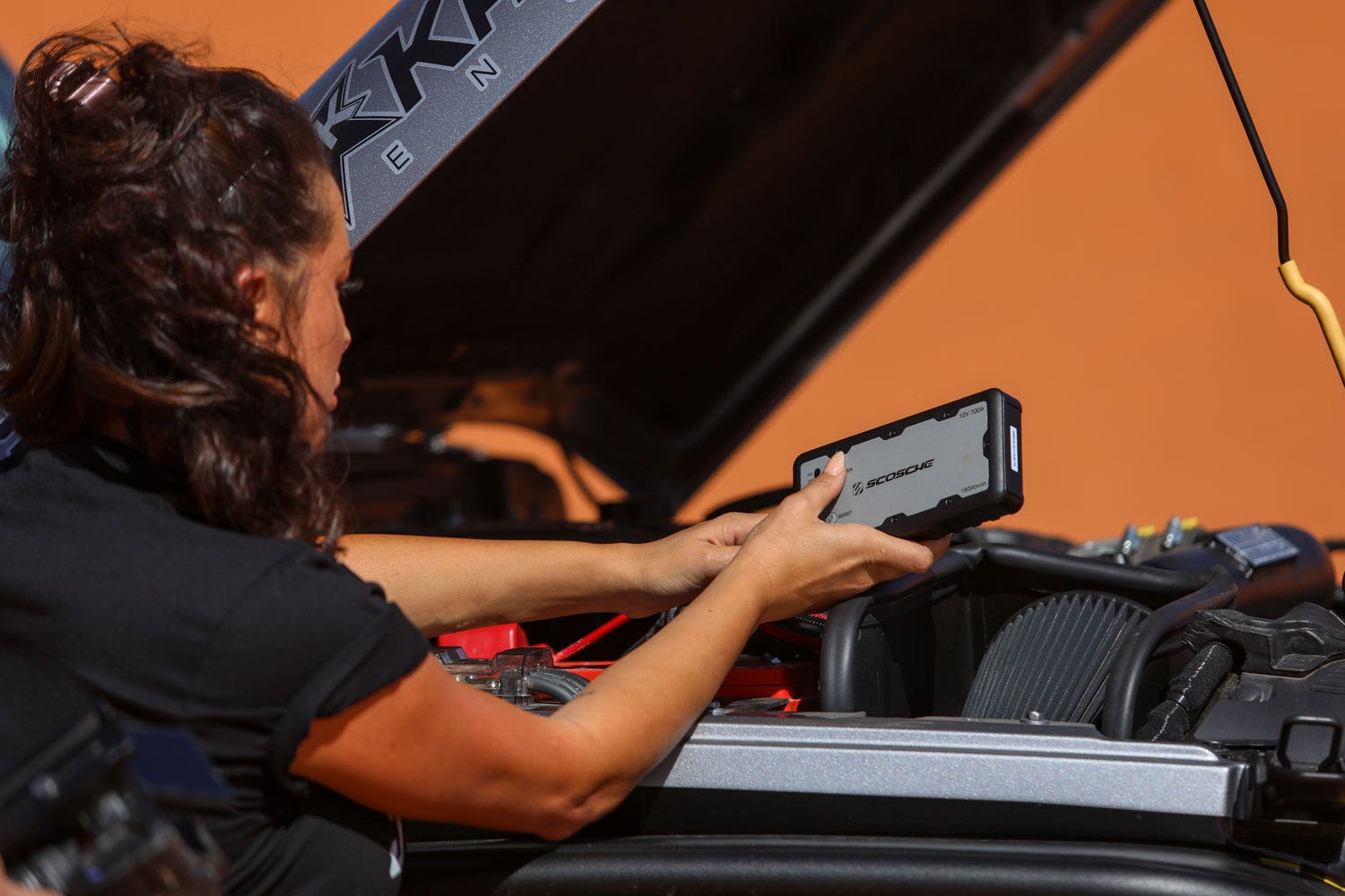 woman using portable car jumper on car battery