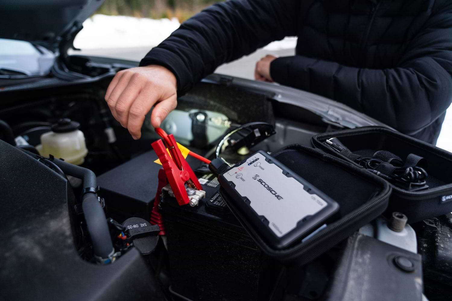 man with portable jump starter on car battery