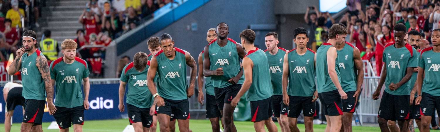 Equipo completo del Liverpool FC posando juntos en el estadio con la camiseta verde de entrenamiento, mostrando unidad y concentración en sesión de entrenamiento