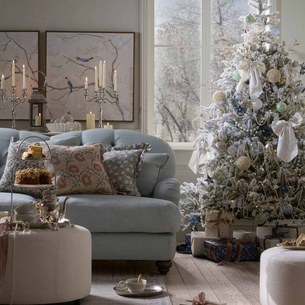 A cosy blue sofa with a silver lit Christmas tree in the background
