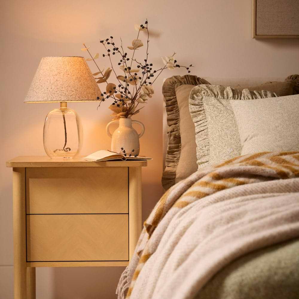 A cosy bed with oak bedside table and bedside lamp