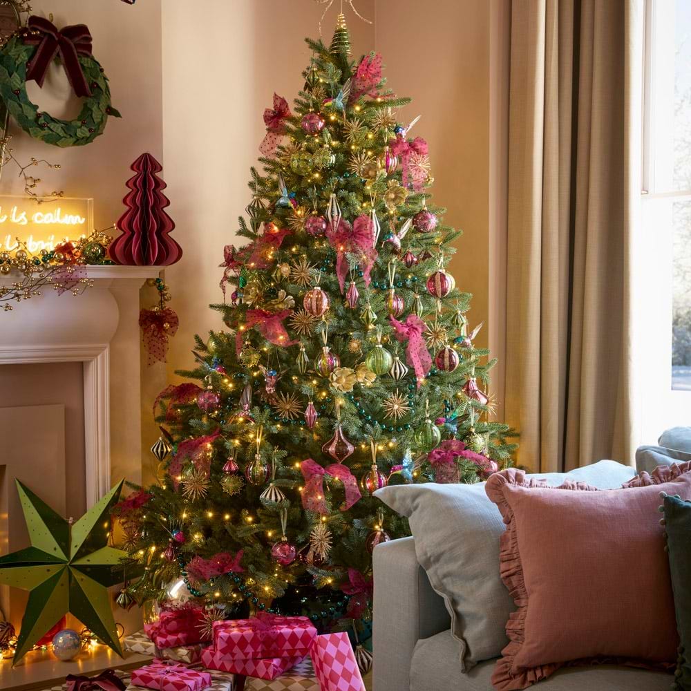 A brightly decorated tree surrounded by pink and green oversized paper star decorations