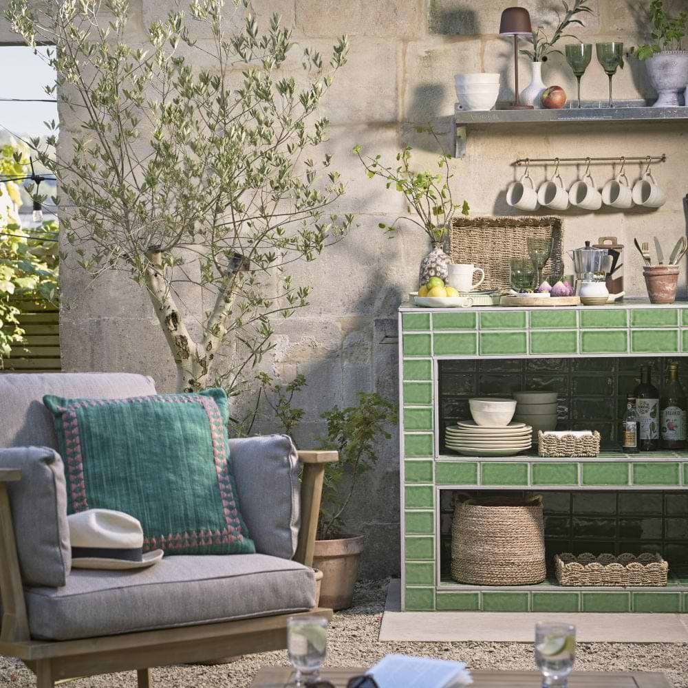 Cox & Cox a courtyard garden with an outdoor kitchen with a cosy garden chair and sidetable in the foreground