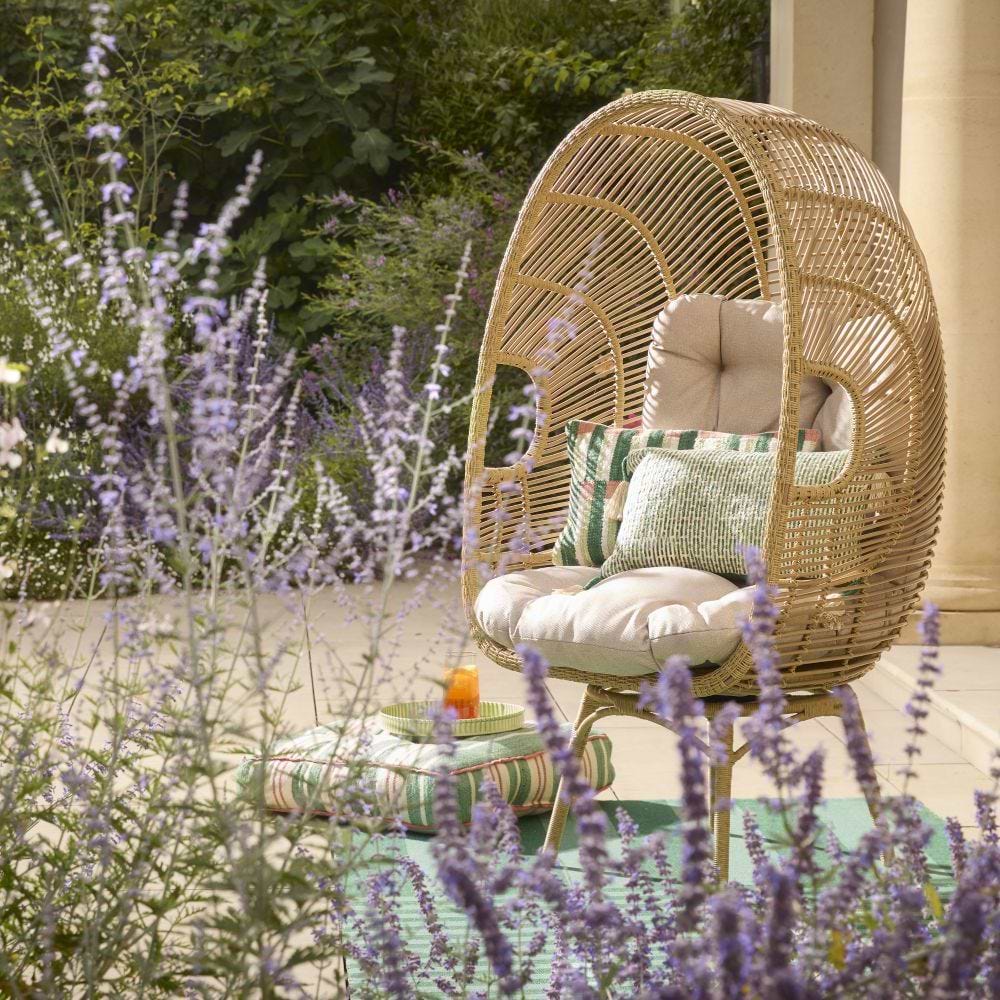 A wicker egg chair pale rattan in a garden setting surrounded by tall purple salvia flowers.