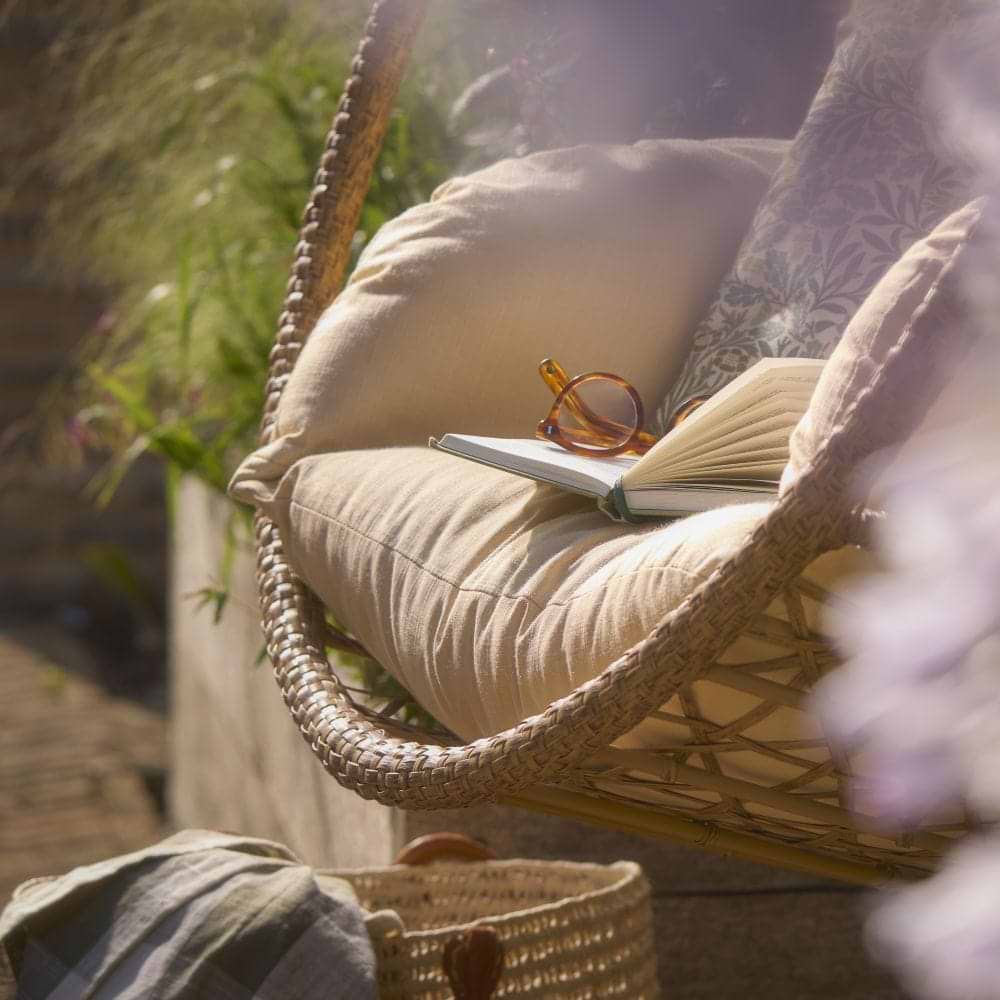 A slightly blurry image of a hanging chair in a garden with a book and sunglasses on the seat srrounded by plants.