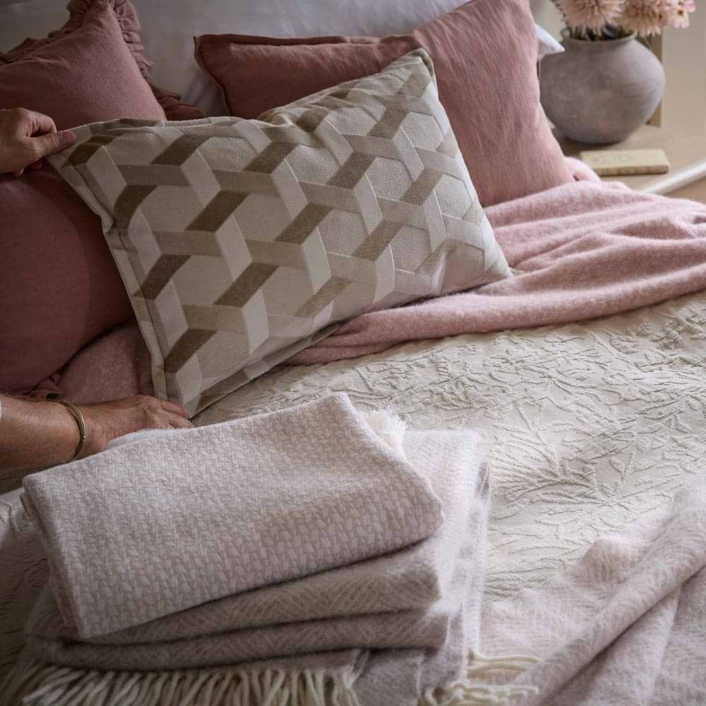 A bed with lots of cushions and throws in cream and pink tones
